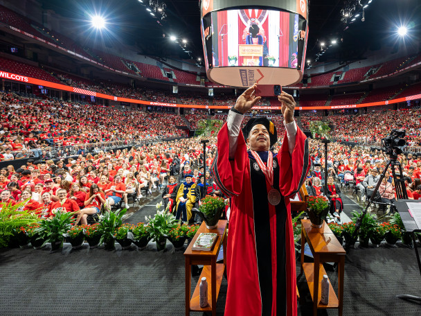 Interim Chancellor Wilcots holds up his phone and takes a selfie of himself and the thousands of students standing in the Kohl Center behind him.