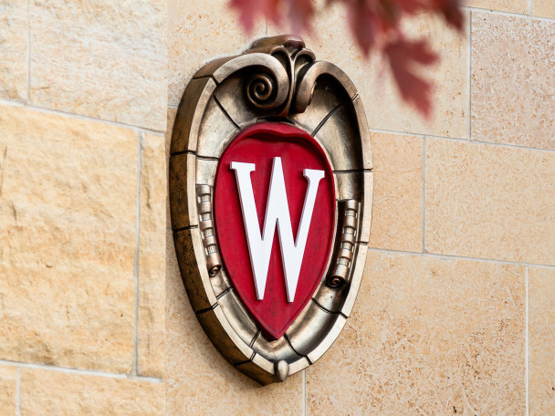 UW–Madison crest logo on the side of a building with red leaves peeking into the top of the photo.