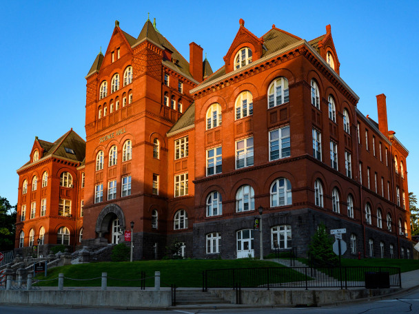 A large red building with many white-framed windows. There is a shaft of sunlight cast across part of the building, which is set against a pure blue sky.