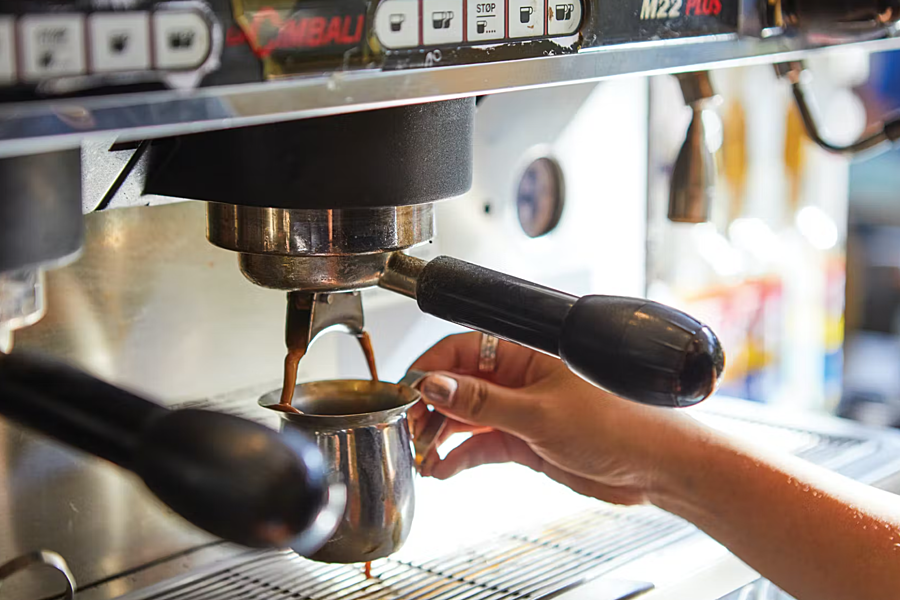 Closeup of espresso dripping into stainless steel cup.