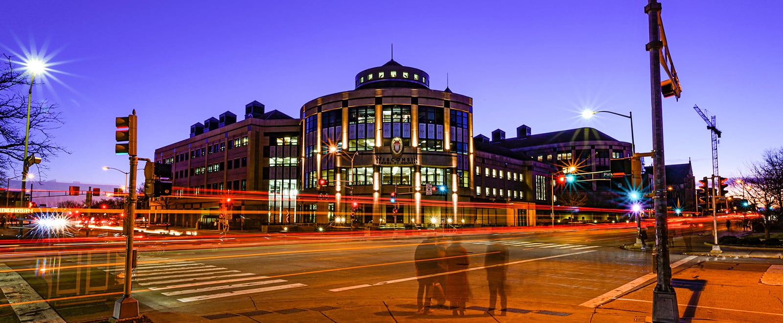 Grainger Hall is pictured during twilight, with streaks of passing traffic and a deep purple sky in the background.