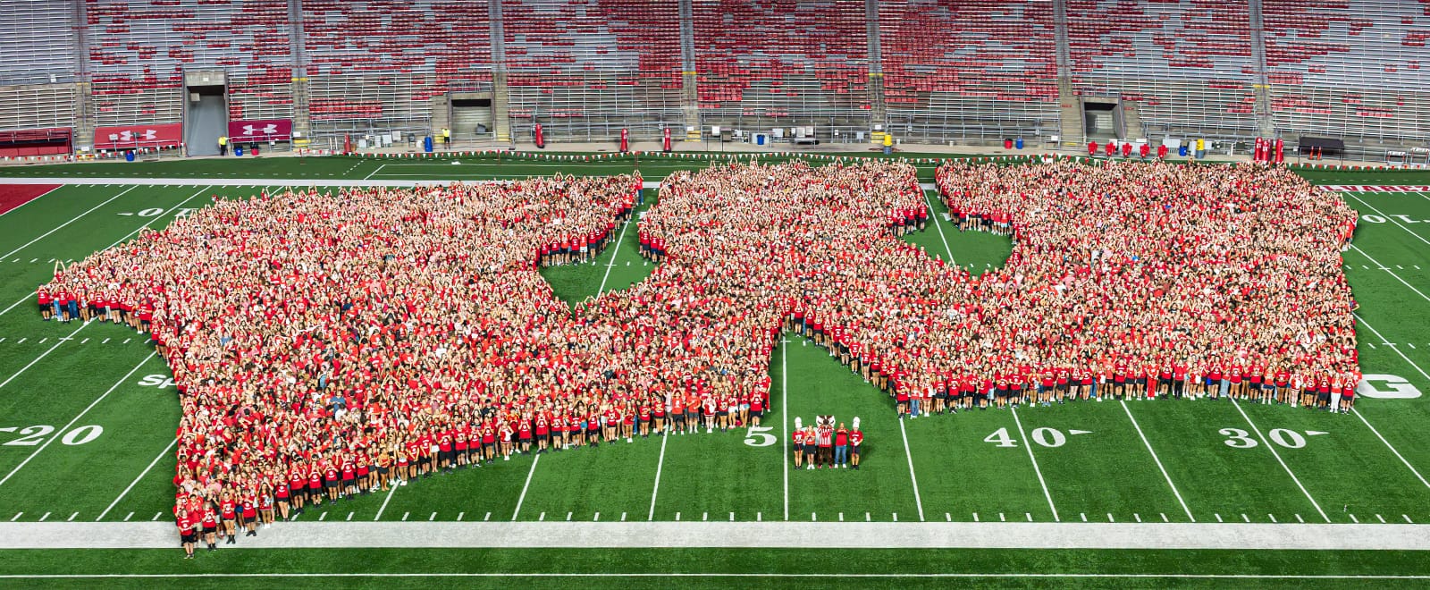 An overhead wide shot of thousands of incoming students wearing red shirts assembled on the field at Camp Randall Stadium to form a massive Motion W logo.