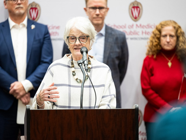 Sigrid Knuti stands behind a podium and speaks into a microphone with UW and Industry leaders behind her.