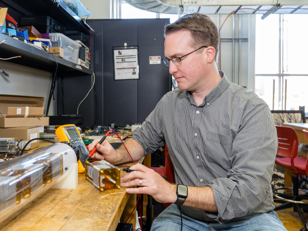 A man sits at a table and works on a small electrical motor.