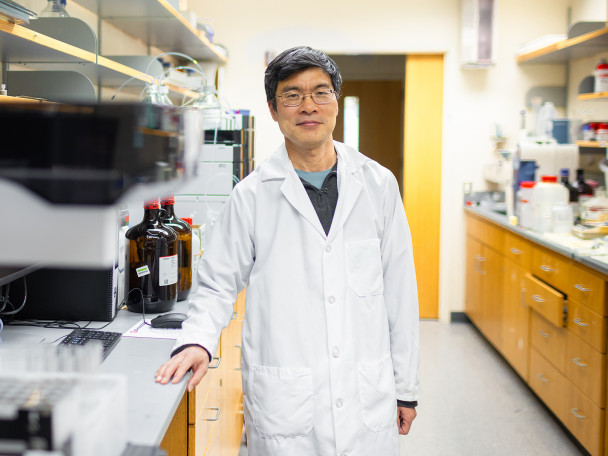 Wearing a white lab coat, a man poses for a picture in his chemistry lab.