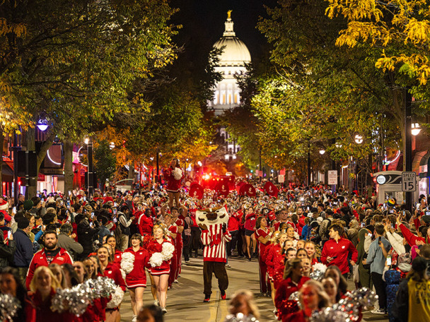 A view of State street at night, crowded with spectators watching the Homecoming parade, the state Capitol visible in the background.