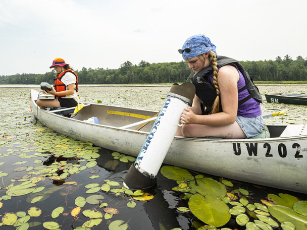 Two women in a canoe use equipment to take samples from the water.