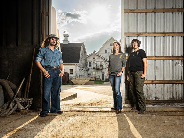 Three UW students are pictured inside of the barn doors of the Dairy Cattle Center.