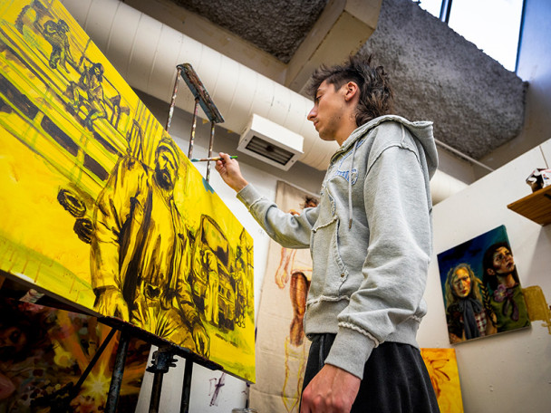 A man uses a brush to put the finishing touches on a yellow painting of a man.