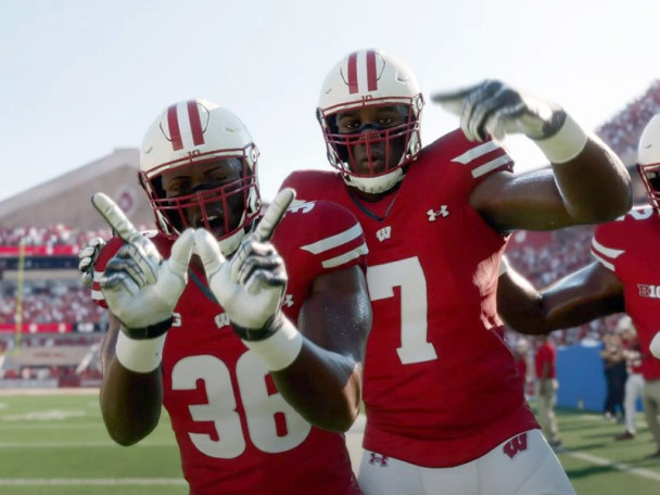 Badger football players smile and flash the 'W' sign on the sidelines of a game at Camp Randall.