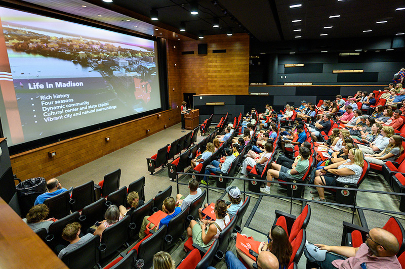 Student sitting in a large lecture hall facing a screen displaying the words life in Madison